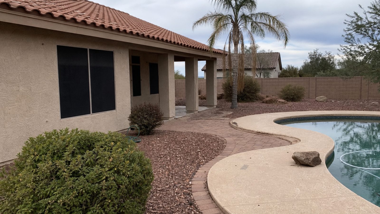 Arizona home exterior with desert landscaping, sun-faded pavers, pool edge, dry heat atmosphere, realistic snapshot