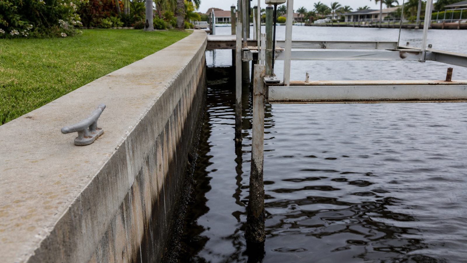 Cape Coral dock cleat and boat lift frame with surface oxidation, waterline staining on seawall, no boat