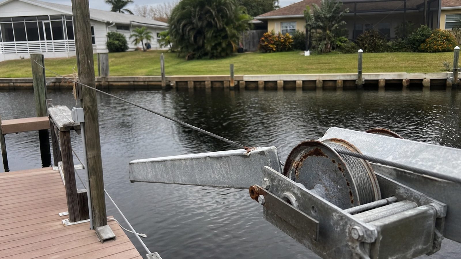 Florida canal dock with boat lift cable showing slight fray near drum and surface-rusted pulley, no boat