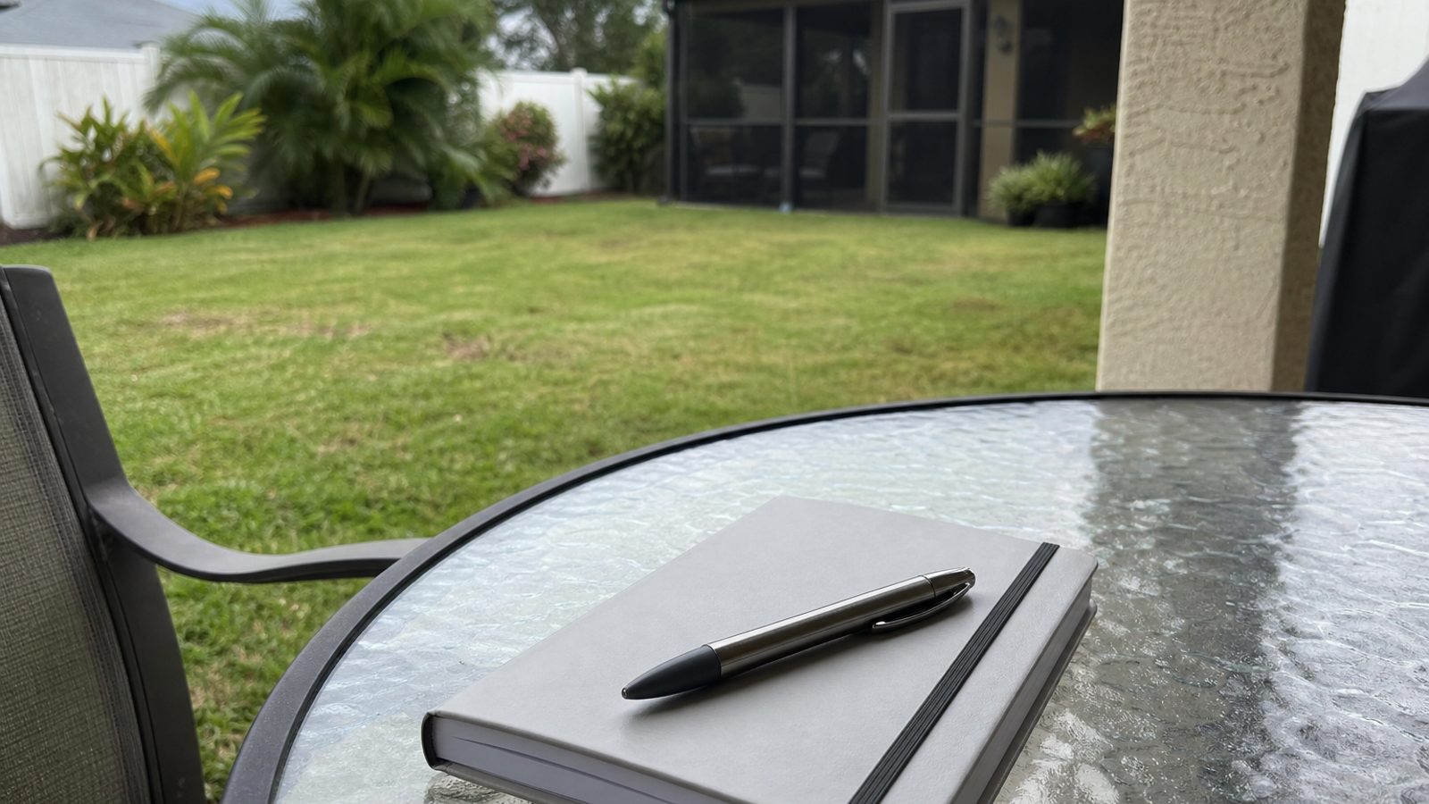 Kitchen table or patio table with homeowner maintenance notebook, printed checklist, blurred Florida yard outside, no readable text